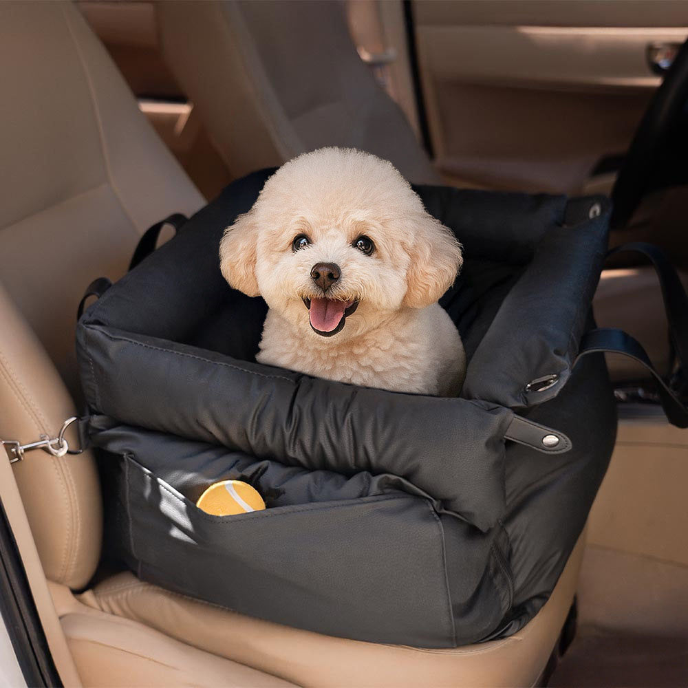 A fluffy small Bichon Frise sitting happily in a black multifunctional pet car seat carrier with a side storage pocket holding a toy ball, keeping pet essentials accessible during travel and outdoor trips.