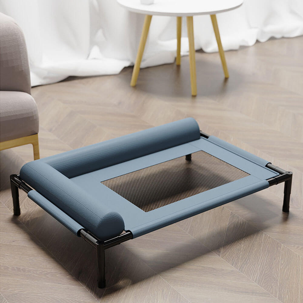 A blue elevated pet cot with breathable mesh center and soft bolster pillows, displayed in a modern indoor living room setting, ideal for dogs and cats, all-season indoor/outdoor use.
