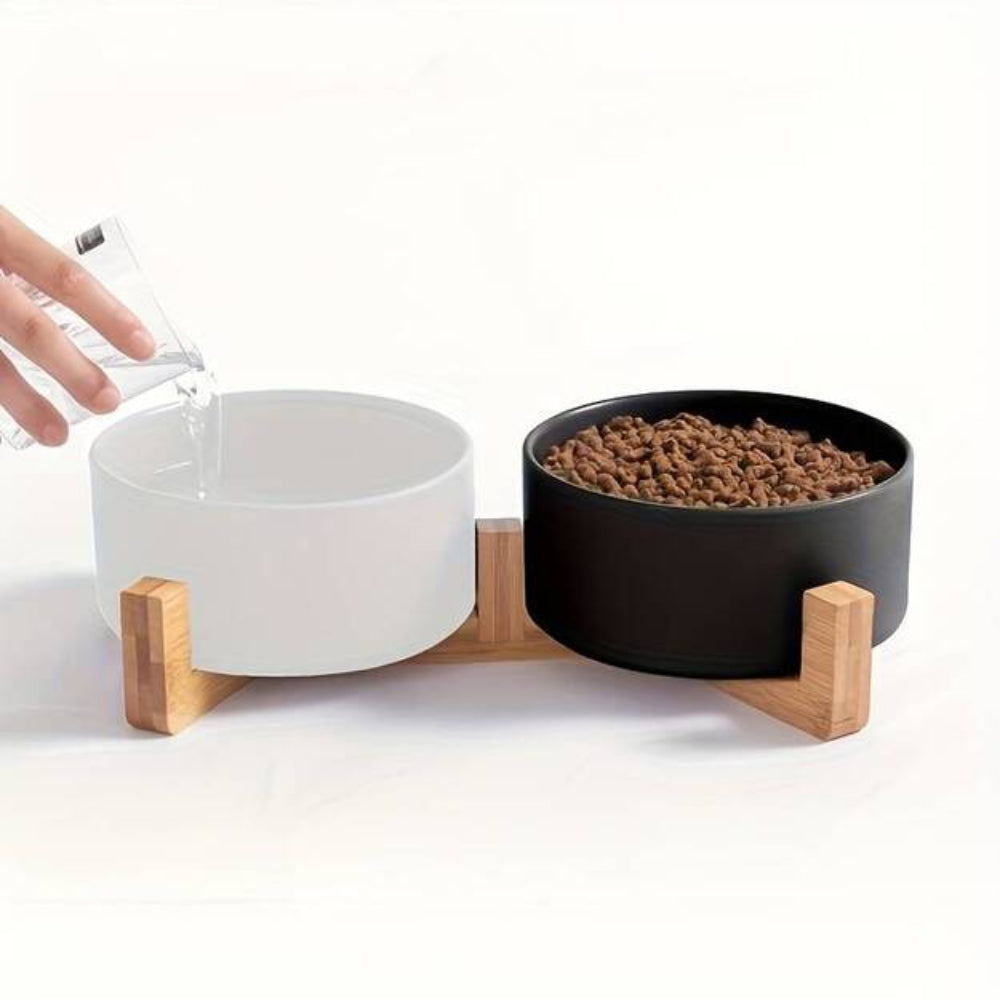 Ceramic pet food and water bowl set on a bamboo stand, featuring a white water bowl and a black food bowl filled with kibble, ideal for cats and dogs, promoting ergonomic feeding.