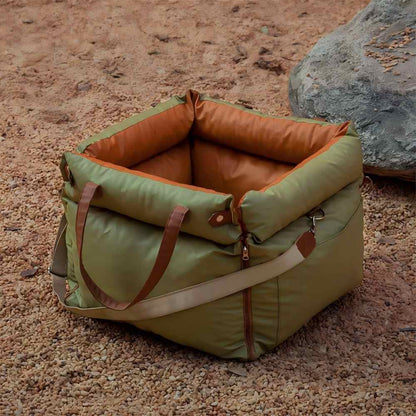 An olive green and orange multifunctional pet car seat carrier placed on gravel, featuring widened leather handles and an adjustable shoulder strap for easy carrying, ideal for camping, hiking, and outdoor adventures with pets.