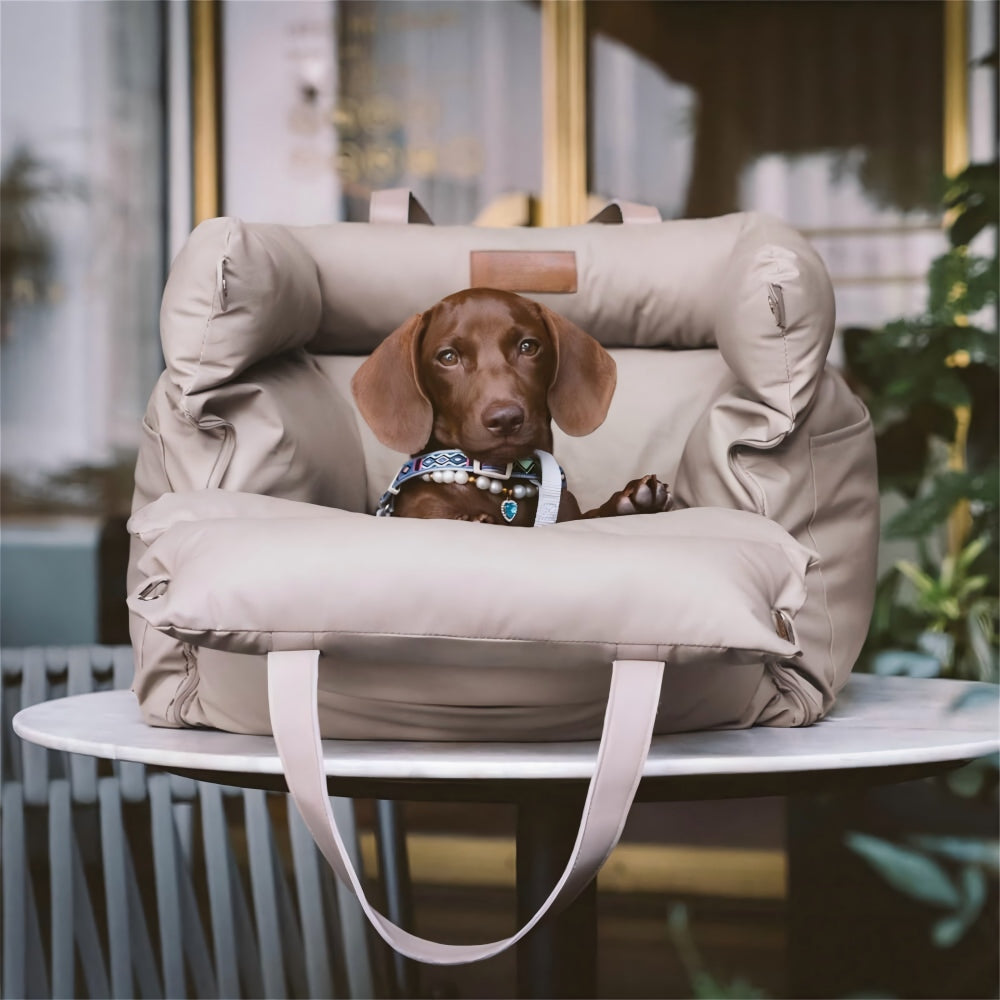 A small brown dog resting in a beige multifunctional pet car seat carrier placed on an outdoor patio table, highlighting its portability and versatility as a pet bed for cafes, camping, and everyday outings.